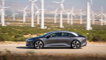 Lucid Air Touring fahrend von der Seite mit Windrädern im Hintergrund im Westen der USA