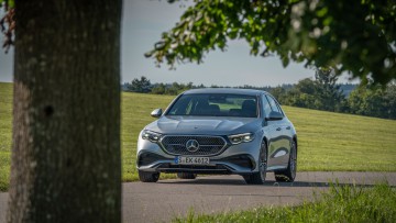 Silberfarbener Mercedes E 450 4Matic von vorn neben einem Spätsommerbaum fotografiert