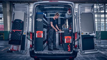 Geöffnete Flügeltür am Ford Transit mit darin stehender Mechanikerin die Werkzeuge aus der integrierten Werkbank entnimmt
