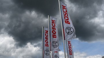 Das Logo des Industriekonzerns und Automobilzulieferers Bosch ist auf Fahnen am Bosch Campus vor dunklen Wolken zu sehen. 
