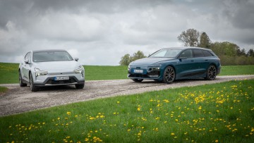 Audi A6 Avant e-tron und Polestar 4 stehen von vorn fotografiert auf einer Anhöhe bei bewölktem Himmel.