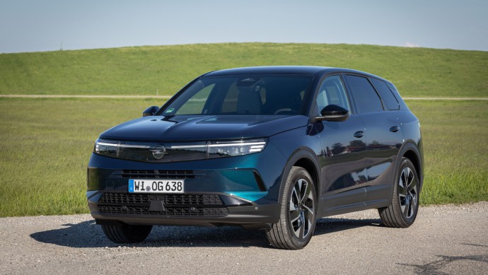 Opel Grandland Hybrid stehend vor grüner Wiese mit leichtem Hügel im Hintergrund