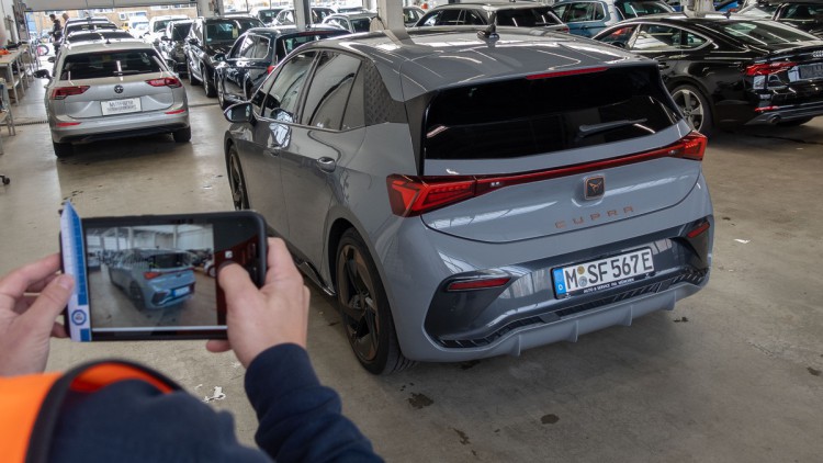 Cupra Born steht in einer Halle zur Leasingrückgabe und wird von einem TÜV-Mitarbeiter von hinten fotografiert