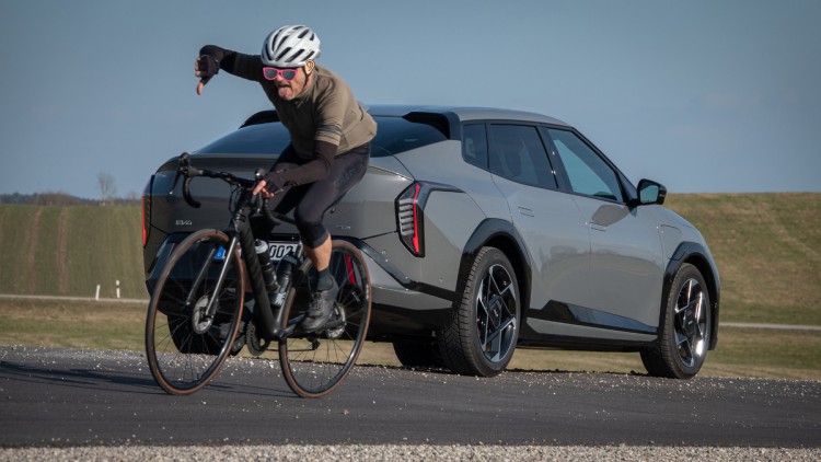 Fahrradfahrer fährt an Kia EV4 Fastback vorbei und zeigt mit Daumen nach unten und hat die Zunge rausgestreckt