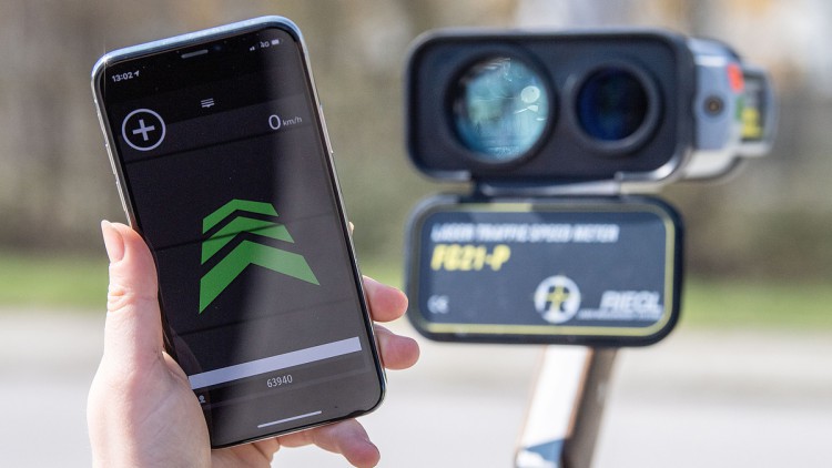 ayern, München: Eine Hand hält ein Smartphone mit einer Blitzerwarnapp, während im Hintergrund ein Radar-Messgerät zu sehen ist. (zu dpa: «Handy-Führerschein soll kommen - Diskussion um Blitzerapps») Foto: Lino Mirgeler/dpa/dpa-tmn +++ dpa-Bildfunk +++