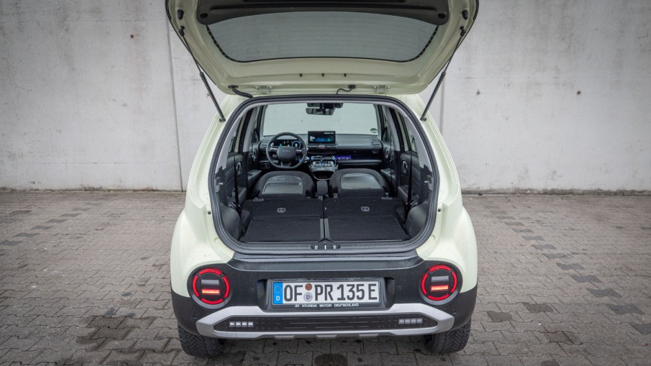 Buttercream Yellow lackierter Hyundai Inster von hinten mit geöffneter Heckklappe fotografiert vor grauer Betonwand