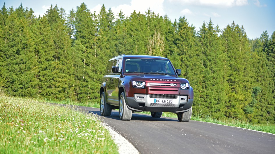 Foto vom Defender 130 auf Asphalt vorm Wald im Spätsommer
