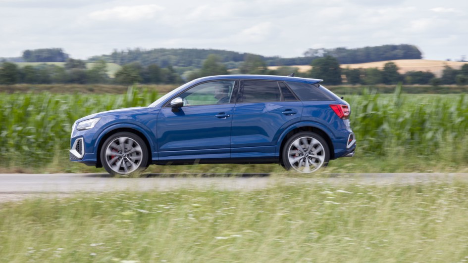 Blauer Audi SQ2 fahrend von der Seite vor gruener Wiese
