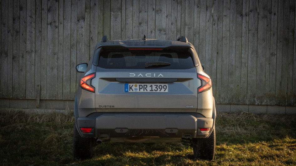 Heckansicht vom Dacia Duster 4x4 vor einer Holzhütte 