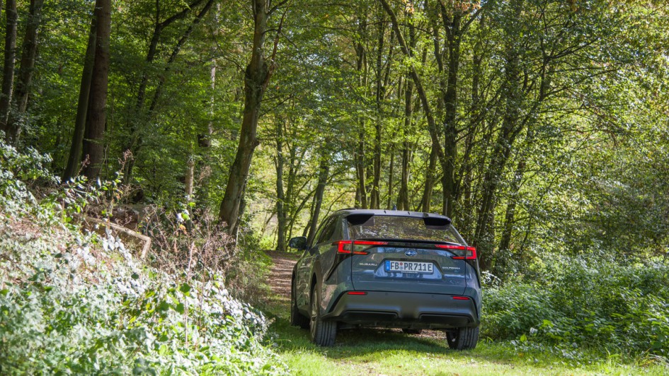 Subaru Solterra steht im Wald, schräg von vor fotografiert