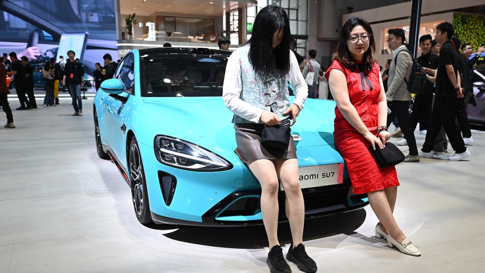 Zwei Frauen stehen an einem Xiaomi SU7 auf einem Messestand.